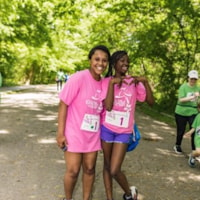 A Girls on the Run Coach and girl participant smiling at the camera wearing a pink 5K shirt